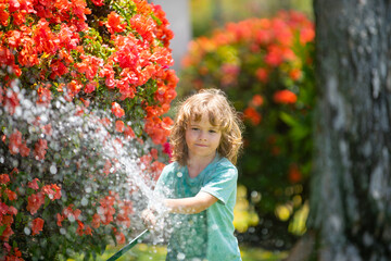 Child watering flowers and plants in garden. Kid with water hose in backyard. Kids gardening. Kids summer fun outdoor at home.