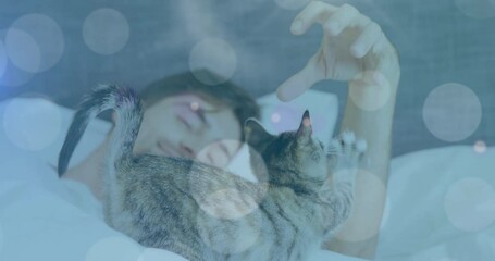 Spots of light against caucasian man playing with his cat while sleeping on the bed at home