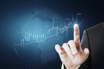 Close up of businessman hand pointing at abstract glowing business chart with globe hologram on blurry blue background. Trade, finance and economy concept. Double exposure.