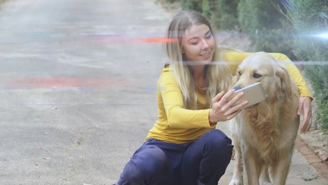 Blue and red light trails against caucasian woman talking a selfie with her dog outdoors