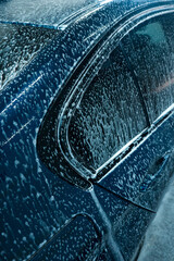 Self-service car wash station. Active foam is cleaning a dirty sedan car. Details of the foam on...