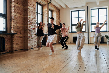 Leader of vogue dance performance group showing new movements to teenagers repeating after him during training in loft studio - obrazy, fototapety, plakaty