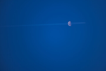 Moon and plane with trail meet in the blue sky