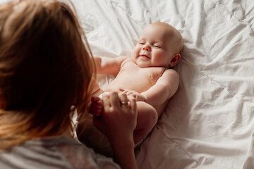 mom kisses the bare feet of a smiling newborn baby lying on the bed. young woman with a baby at home