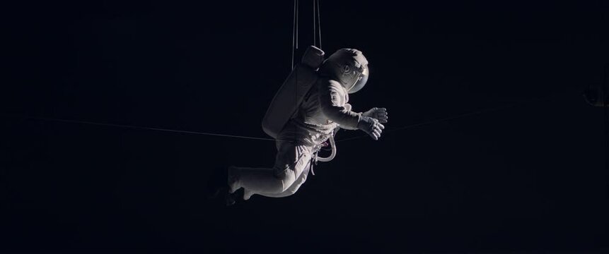 Behind the scenes of commercial shot - Caucasian female astronaut stuntwoman hanging on a wires, wearing a spacesuit