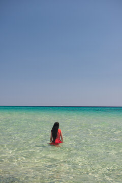 art portrait of woman in red dress standing in tropical turquoise italian ocean in summer