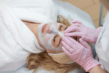 Facial peeling mask, beauty spa, skin care. Woman getting facial treatment by beautician at SPA salon, closeup - obrazy, fototapety, plakaty