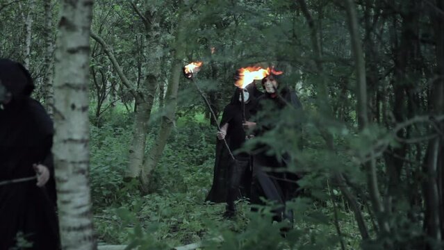 An unrecognizable man hides from a cult of evil hooded druids in the woods who are about to perform a sacrifice ritual