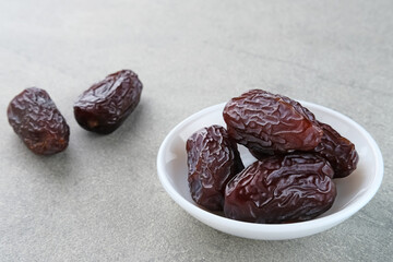 Fresh Medjool Dates Fruit served in small plate on grey background. Close up. Ramadan kareem. 
