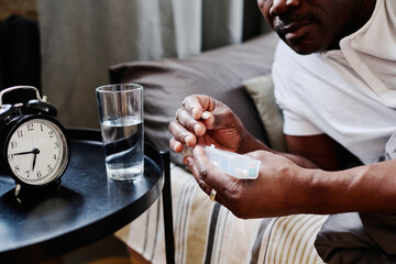 Hands of contemporary senior black man holding long plastic container with pills while taking medicaments after sleep in the morning
