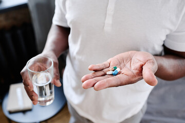 African American senior man with glass of water and three pills on hand going to take medicaments prescribed by his physician