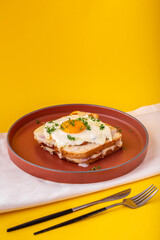 Croque madame sandwich with ham, melted cheese and a fried egg on the table on the yellow background. French sandwich. Delicious traditional French breakfast. Hot sandwich. French cuisine. Copy space.