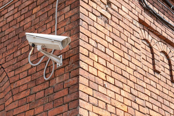 Closed-circuit television camera mounted on brick wall. CCTV security camera outdoors.