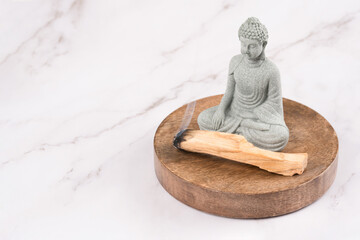 Burning palo santo sticks with Buddha statue in a meditation room on white marble background. Zen...