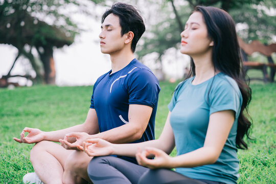 Image of young Asian couple meditating together on the grass