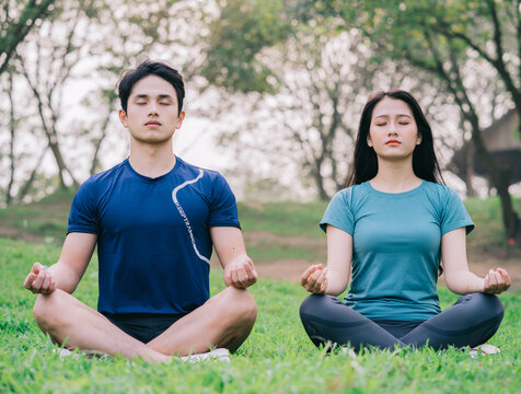 Image of young Asian couple meditating together on the grass