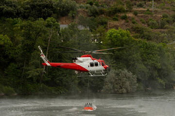 A helicopter pilot scoops up water with a bucket from a river to blow off the mountain