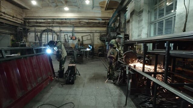 A welder and a metal cutter in the workshop of a metalworking workshop prepares steel parts. Sparks.Workers work at the factory, the welder prepares, the workflow in the shop