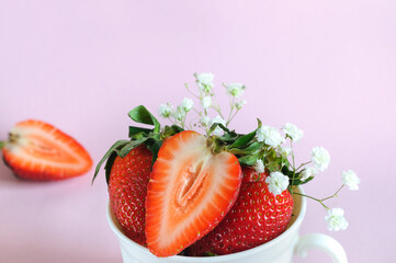 Ripe strawberries in a white mug, close-up with flowers on a pink background. Selective focus. copy space from above