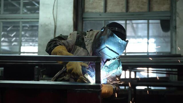 A worker cooks metal on a welding machine in production. a worker with a welding machine to cook parts