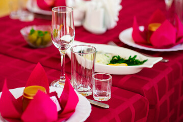 Background of beautiful served table with Red tablecloth and napkins, white china, gold cutlery, spruce tree branches. Top view. Holiday setting, Christmas mood.