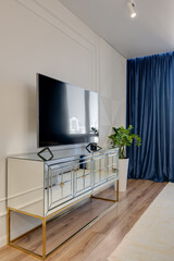 Mirrored TV stand in the interior with a blue curtain and light walls