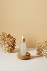 Transparent dropper bottle on wooden podium with dry flowers on pastel beige background. Aesthetic,...