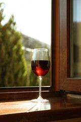 Glass of red wine stands on wooden windowsill