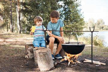 Children sitting around a campfire in forest in summer. Family picnic outdoors. Camping life....