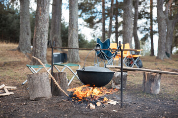 Cooking in cauldron on open fire in nature. Bowler on bonfire in forest. Pot from cast iron on...