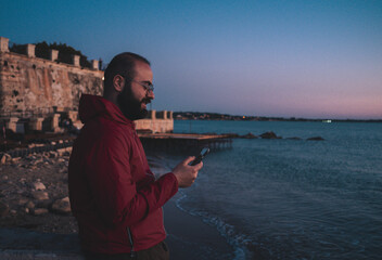 boy uses smartphone at sunset in the harbour