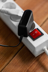 electricity, energy and power consumption concept - close up of socket with plugs, charger and red switch button on wooden floor
