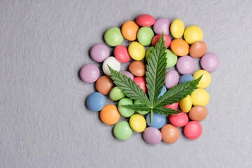 Cannabis leaf with colorful candy confetti close up. Marijuana sweets with CBD and THC on gray .background. Top view, flat lay.