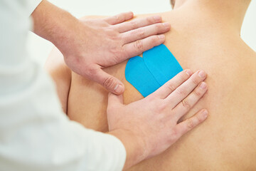 kinesiology therapeutic strip tape applying on male back for pain relief