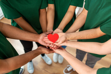 charity, support and volunteering concept - close up of volunteers's hands holding red heart at...