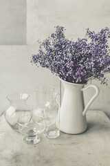 large bouquet of purple gypsophila flowers in a white jug and many glass jars and bottles on a white background. art image, floral still life, vertical, selective content