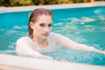 Portrait of a beautiful girl with wet hair floating in the pool, wearing a white shirt. Rest in the...