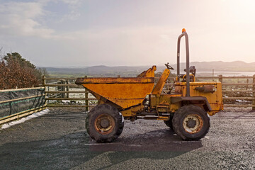 Old rusty dumper track parked on a parking lot in a country side. The vehicle is yellow color has many scratches. Warm sunny day. Cloudy sky. Construction and repair equipment for rent concept.