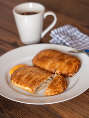 Serving of two ham and cheese pies on a white plate on wooden table. Simple food concept. Pastry product for lunch.
