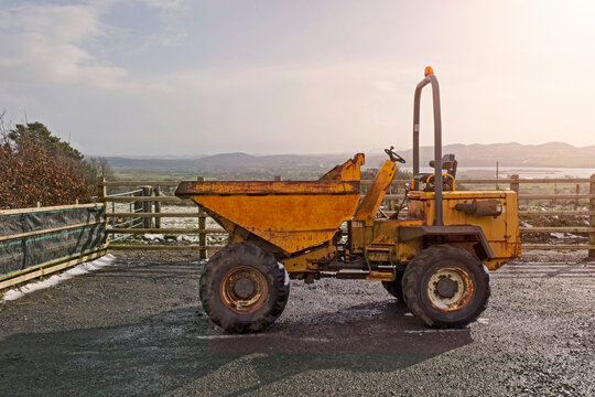Old rusty dumper track parked on a parking lot in a country side. The vehicle is yellow color has many scratches. Warm sunny day. Cloudy sky. Construction and repair equipment for rent concept.