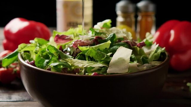 Green lettuce leaves fall into a plate. Salad bowl on a wooden table on a dark background with spices and bell peppers.