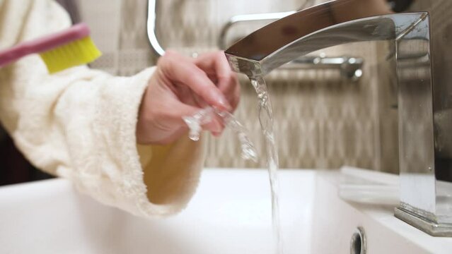 Close-up of unrecognizable caucasian young woman toothbrushing her kappa aligner under running water in bathroom sink. Care of dental accessories