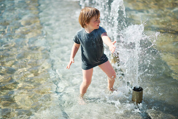 Outdoor portrait of happy little boy playing inside of city fountain on a hot summer day