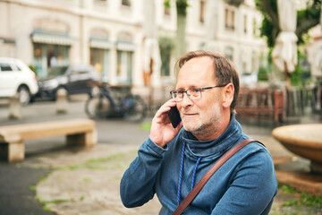 Outdoor portrait of middle age man talking on the phone, wearing glasses and blue sweatshirt, holding smartphone next to ear