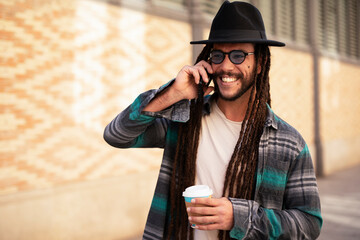 Handsome guy drinking coffee while walking in the street. Modern fashion man using the phone.
