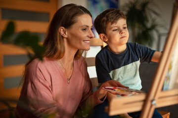 Mother and son painting at home. Little boy drawing with mom in living room