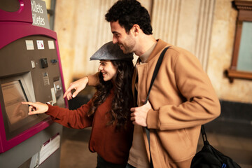 BEautiful loving couple buying train ticket at self service vending machine on the station. Happy woman and man travel together