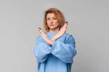 Serious middle age woman with curly blonde hair crossing arms and palms doing negative sign,...
