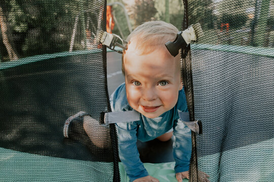 Cheerful, happy child, toddler jumping on a trampoline. Little boy looking threw the trampoline safety net entrance. Children playing outdoors in summer nature.