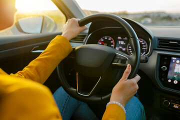 Close-up of a female hands in yellow suit driving a car outside the city. Traveler girl on car...